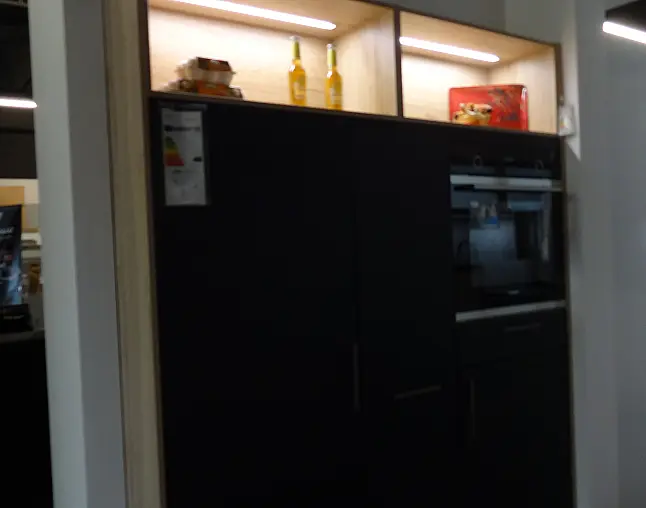 Schwarzer Küchenmöbelblock mit beleuchtetem Regal oben, zwei Flaschen und einer roten Box darauf.