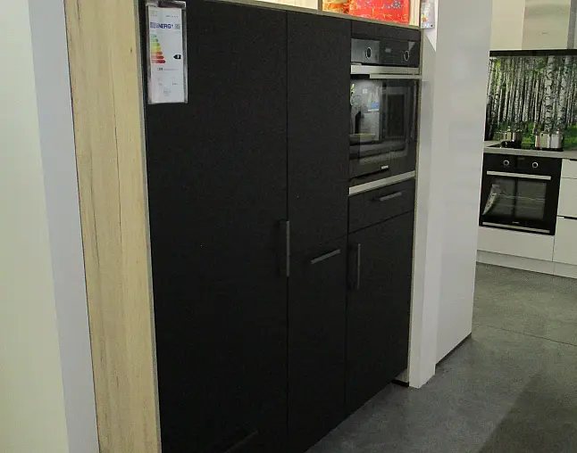 Schwarze Küchenschränke mit eingebautem Ofen und Mikrowelle neben einem hellen Holzpaneel.