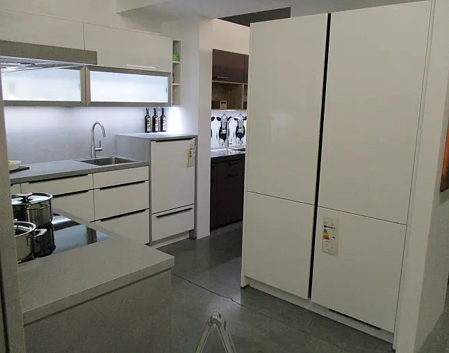Moderne weiße Küche mit Glaskochfeld, Spüle, Kühlschrank und großen Schränken.