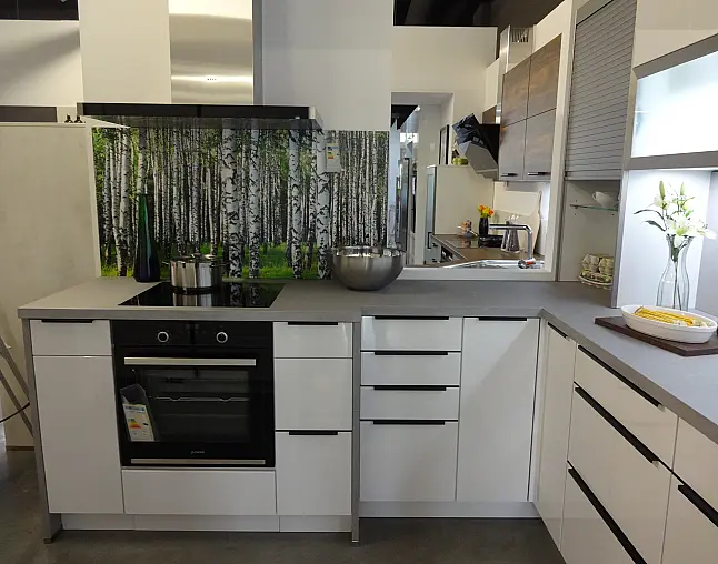 Moderne weiße Küche mit grauen Arbeitsflächen, Backofen und Birkenwald-Motiv als Rückwand.