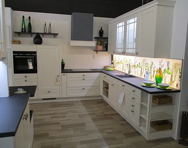 Moderne weiße Küche mit schwarzen Arbeitsflächen und beleuchtetem Rückwand mit Pflanzenmotiven.