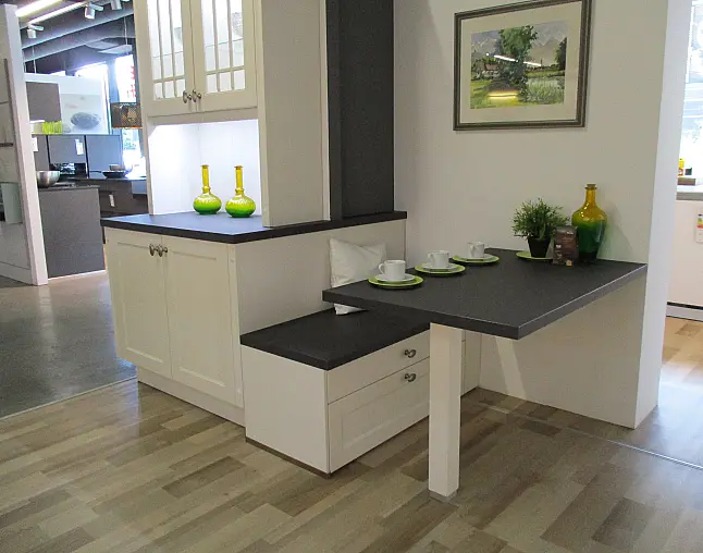 Moderne Küche mit grauer Arbeitsplatte, weißem Schrank, Sitzbank und gedecktem Tisch mit Tassen und Deko.