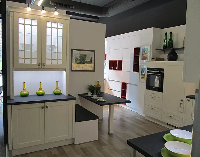 Moderne Küchenzeile in weiß mit schwarzen Arbeitsplatten, Vitrinenschrank, Esstisch und Dekoration.