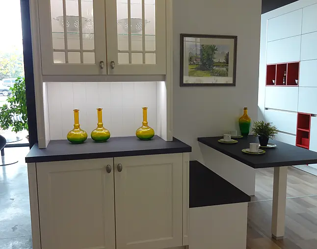 Modern kitchen corner with white cabinets, black countertop, green-yellow vases, and a small dining area.