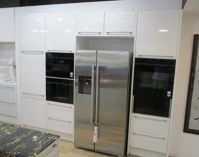 Moderne Küche mit weißen Hochglanzfronten und seitlichem Edelstahl-Kühlschrank mit Doppelöffnung.