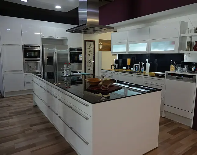 Moderne Küche mit weißer Insel, schwarzen Arbeitsplatten und Edelstahlgeräten auf Holzboden.