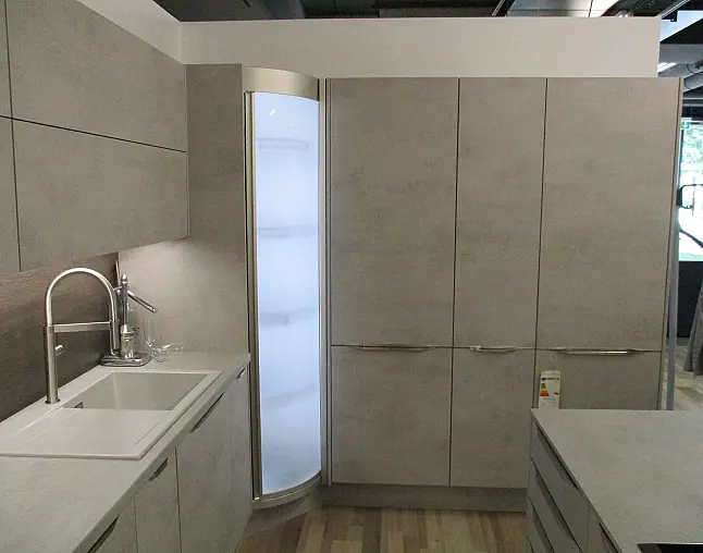 Moderne Küchenzeile in Betonoptik mit Spüle, gebogenem Glasregal und Schränken.