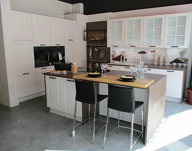 Moderne weiße Küche mit Kücheninsel, schwarzen Barhockern und Glasfrontschränken.